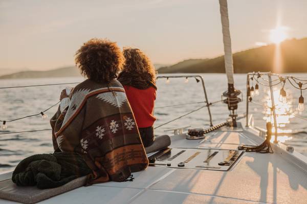A couple sit near the bow of a sail boat and watch the sun set