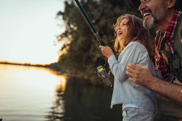 A man helps a child reel in a fish