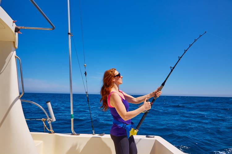 A woman reels in a fish on a boat
