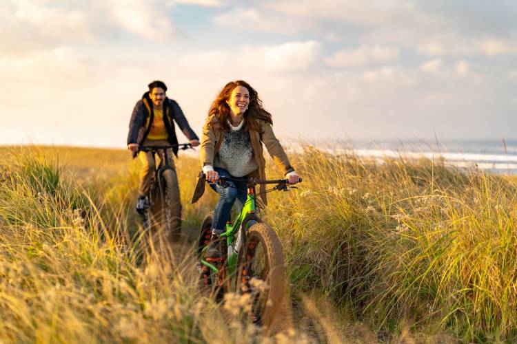 Two people ride bikes along a shore path