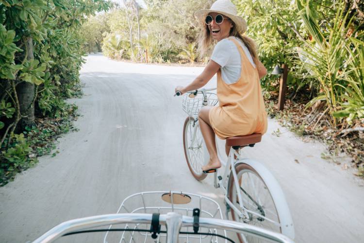 A woman rides a bike through a trail surrounded in green foliage 